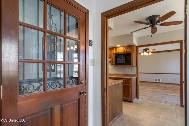 kitchen featuring light tile patterned floors, visible vents, brown cabinetry, and black microwave