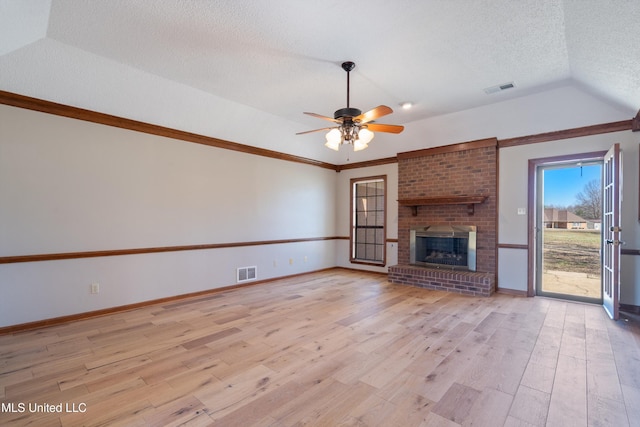 unfurnished living room with light wood-type flooring, visible vents, a textured ceiling, and a brick fireplace