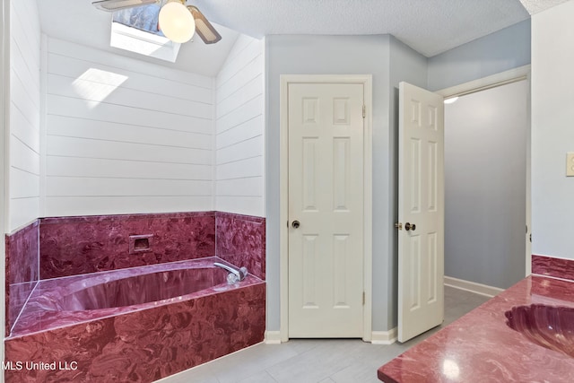 bathroom with tile patterned flooring, ceiling fan, a garden tub, a textured ceiling, and a sink