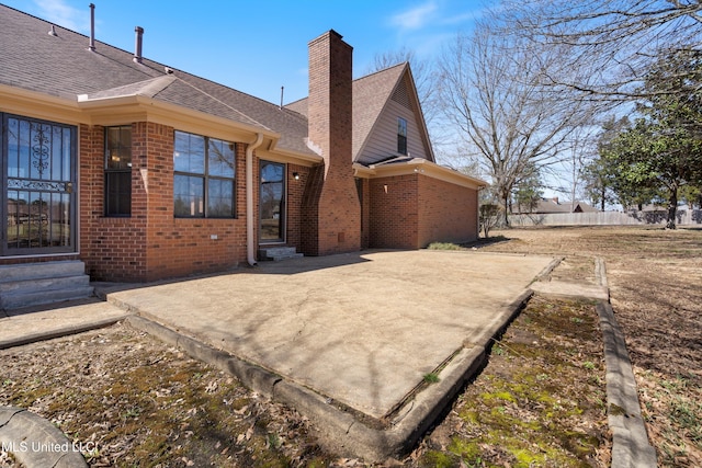 back of house with entry steps, a shingled roof, brick siding, a chimney, and a patio area