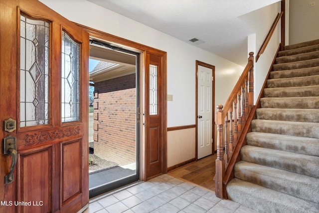 foyer featuring light tile patterned flooring, visible vents, a textured ceiling, and stairs