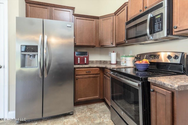 kitchen with stone finish floor, brown cabinets, and stainless steel appliances