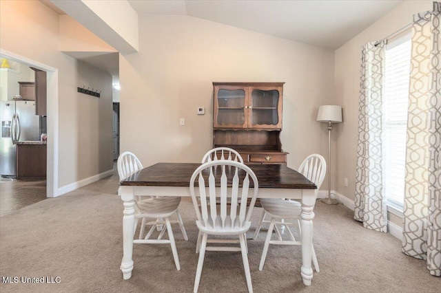 dining room with baseboards, vaulted ceiling, and light colored carpet