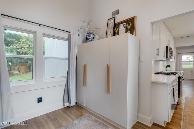 kitchen featuring visible vents, light countertops, white cabinets, light wood-style floors, and stainless steel appliances