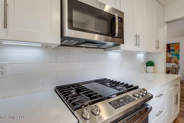 kitchen with white cabinets, stainless steel appliances, light stone counters, and decorative backsplash