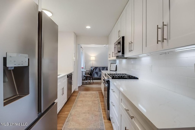 kitchen with light wood-style floors, backsplash, stainless steel appliances, and white cabinetry
