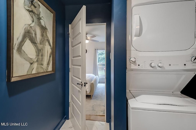 laundry area featuring stacked washer / drying machine, laundry area, marble finish floor, a ceiling fan, and baseboards