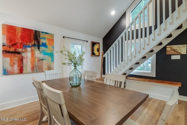 dining area with baseboards, lofted ceiling, wood finished floors, and stairway