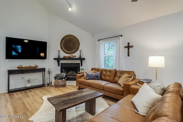 living area with light wood-style floors, a fireplace with raised hearth, and lofted ceiling