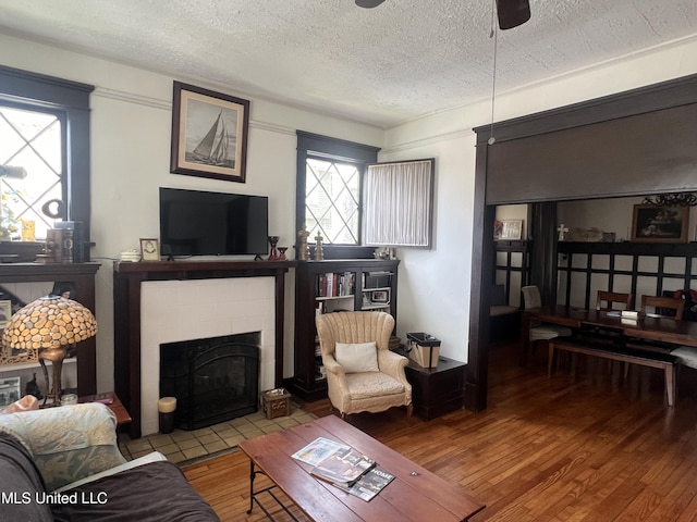 living room featuring a tiled fireplace, a textured ceiling, ceiling fan, and wood finished floors