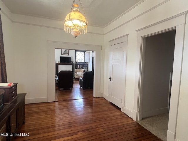 corridor featuring hardwood / wood-style floors, an inviting chandelier, baseboards, and ornamental molding