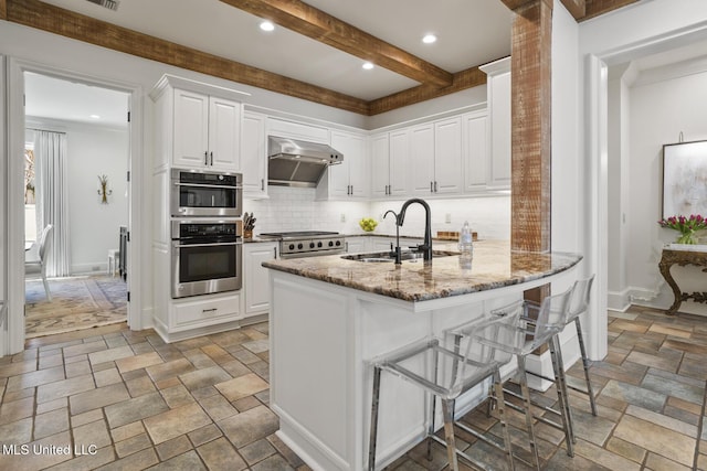 kitchen with stone tile flooring, stainless steel double oven, a sink, range, and under cabinet range hood