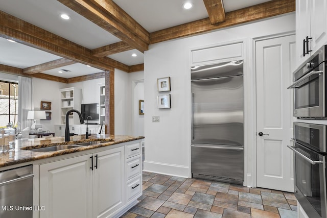 kitchen featuring appliances with stainless steel finishes, stone countertops, white cabinetry, a sink, and baseboards