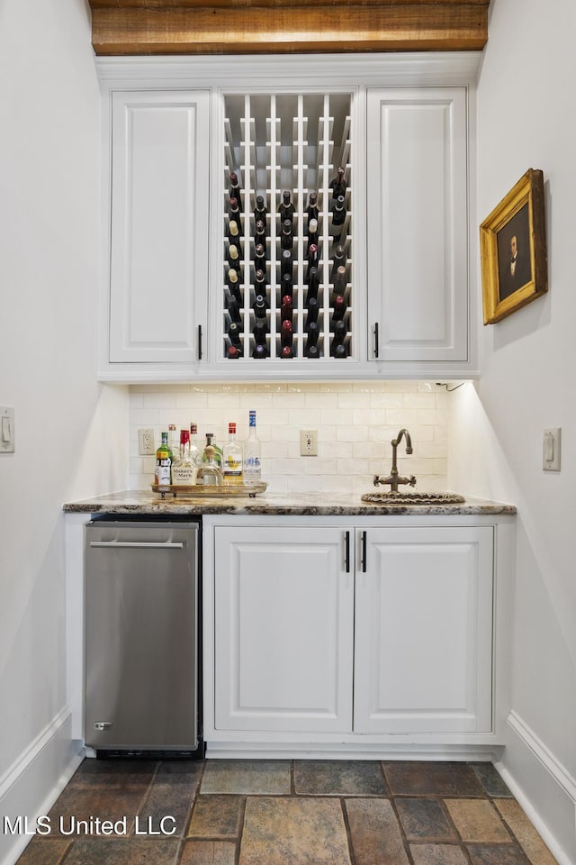 bar featuring stone tile flooring, indoor wet bar, a sink, and decorative backsplash