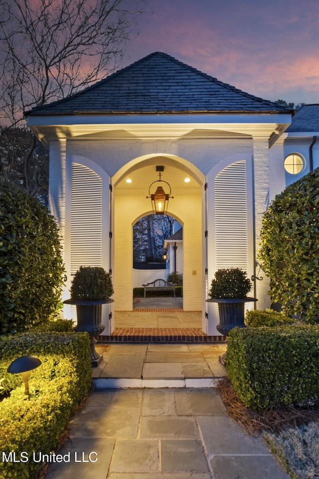 exterior entry at dusk with covered porch and a high end roof