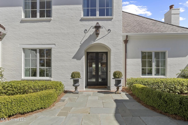 entrance to property with french doors, a chimney, a shingled roof, and brick siding