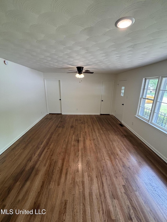 unfurnished living room with baseboards, a ceiling fan, and dark wood finished floors