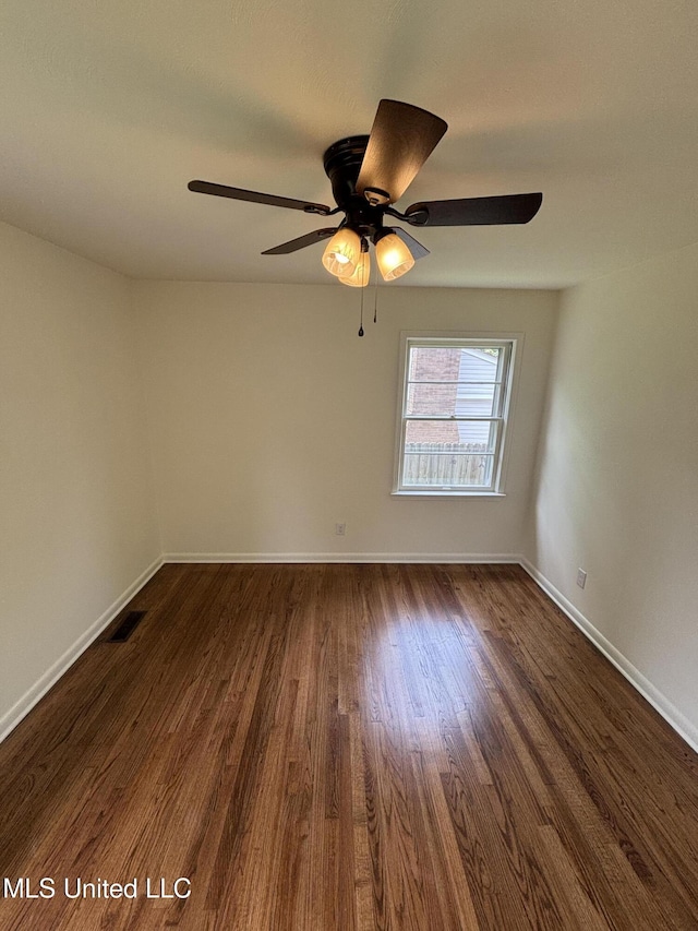 spare room featuring dark wood-type flooring, a ceiling fan, baseboards, and visible vents