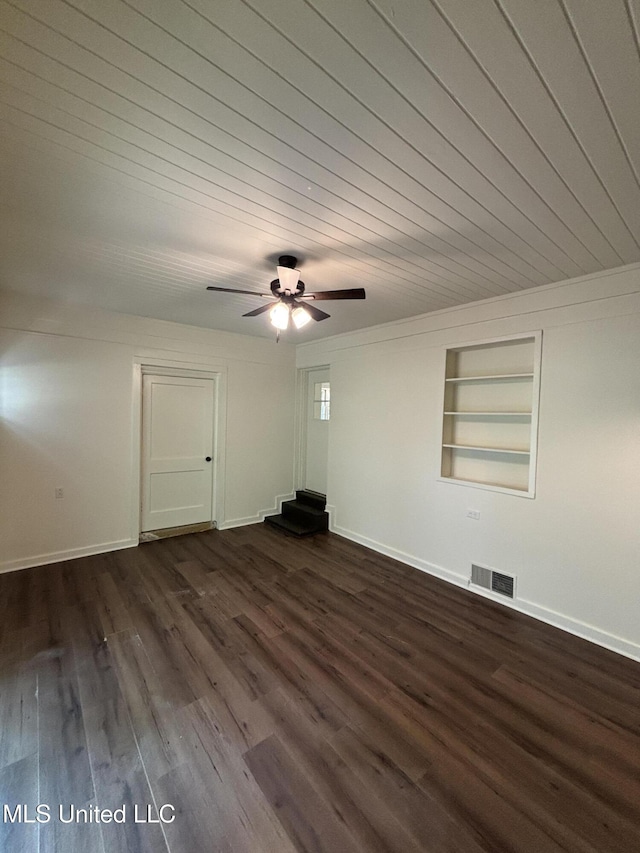 empty room featuring built in features, a ceiling fan, baseboards, dark wood-type flooring, and visible vents