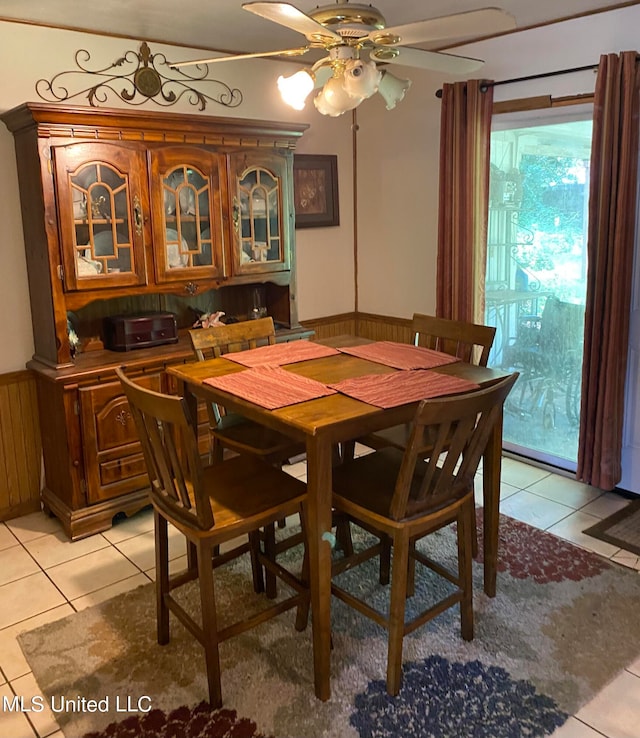 dining area featuring ceiling fan, light tile patterned floors, and wooden walls