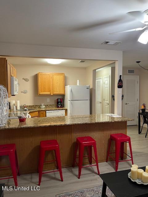 kitchen featuring light stone counters, white appliances, a kitchen bar, and kitchen peninsula