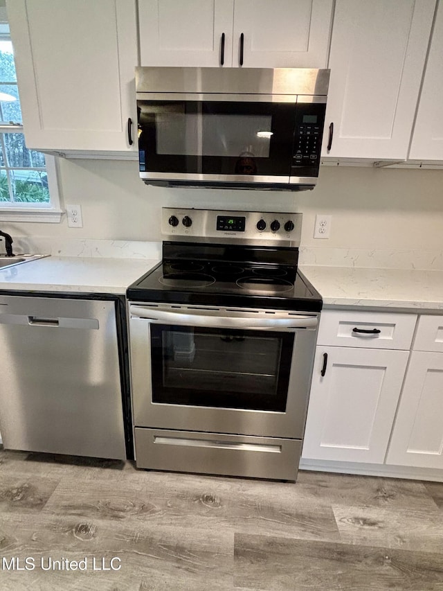 kitchen with light stone countertops, stainless steel appliances, white cabinets, and light wood-type flooring