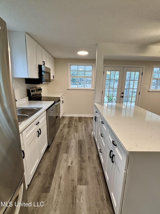 kitchen featuring sink, white cabinetry, light stone counters, wood-type flooring, and stainless steel appliances