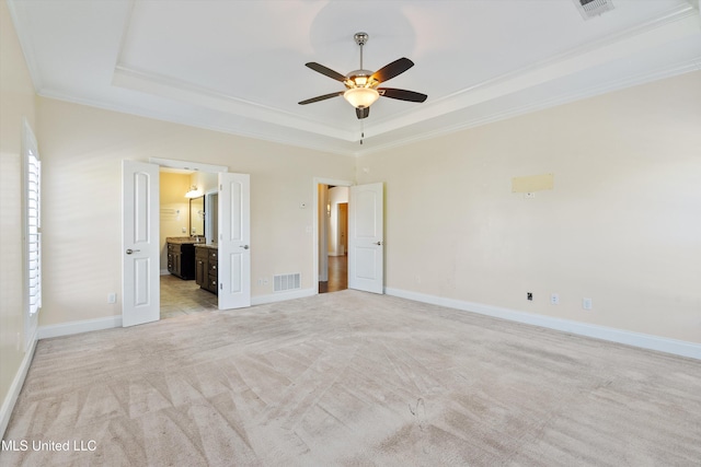 unfurnished bedroom with crown molding, light carpet, ensuite bath, and a tray ceiling