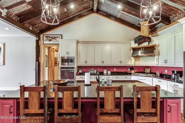 kitchen featuring stainless steel appliances, wall chimney range hood, a chandelier, a center island, and lofted ceiling
