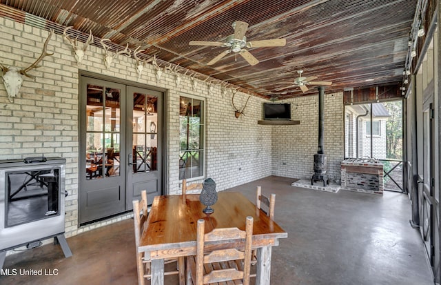dining room with french doors, a wood stove, ceiling fan, and brick wall