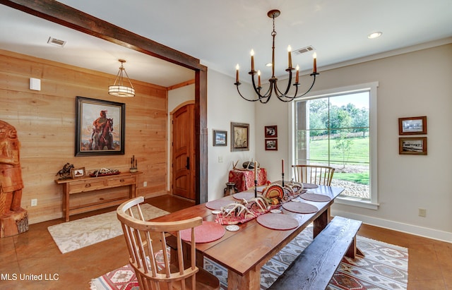 dining space with tile patterned flooring, beam ceiling, a notable chandelier, and wood walls