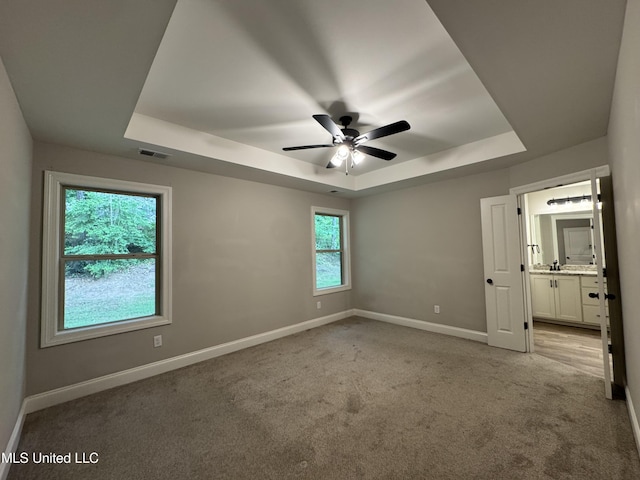 unfurnished bedroom with a tray ceiling, visible vents, light carpet, and baseboards