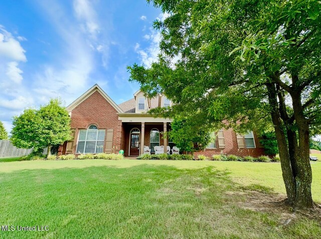 view of front of home with brick siding, a porch, a front yard, and fence