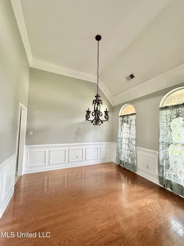 empty room featuring wood finished floors, visible vents, lofted ceiling, ornamental molding, and a notable chandelier