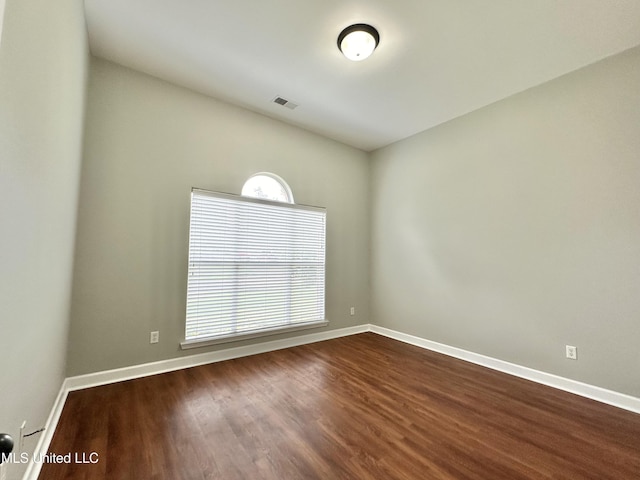 unfurnished room with dark wood-style floors, visible vents, and baseboards