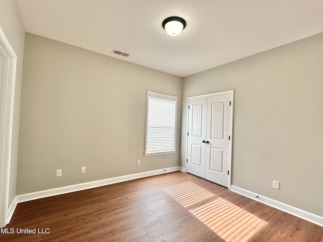 unfurnished bedroom featuring visible vents, baseboards, a closet, and wood finished floors