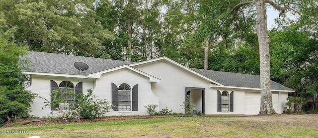 ranch-style home with an attached garage, brick siding, a front yard, view of wooded area, and a shingled roof