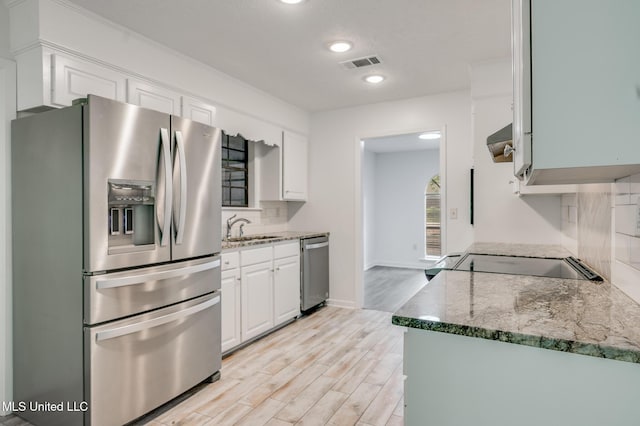 kitchen with stainless steel appliances, a sink, light wood-type flooring, white cabinets, and stone counters