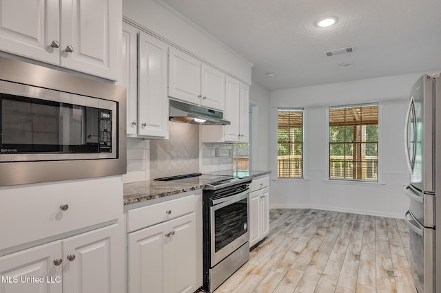 kitchen with under cabinet range hood, appliances with stainless steel finishes, white cabinetry, decorative backsplash, and recessed lighting