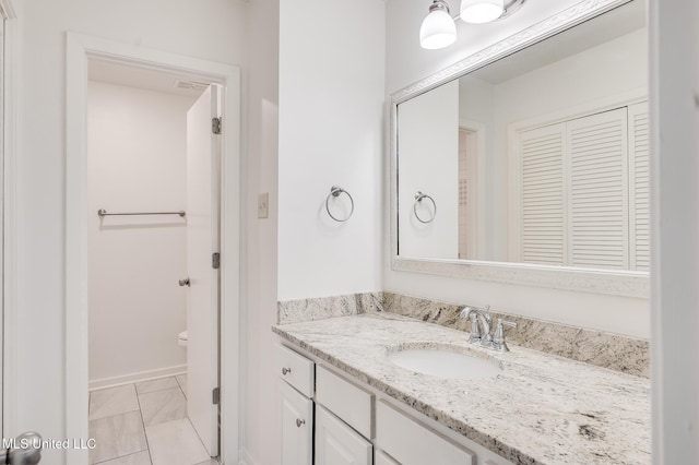 bathroom with vanity, marble look tiles, toilet, and baseboards