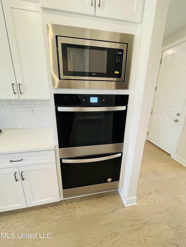 interior details with decorative backsplash, white cabinetry, stainless steel microwave, and light hardwood / wood-style flooring