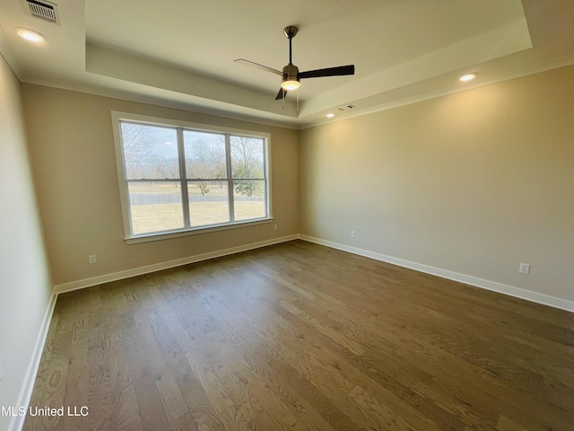 empty room with hardwood / wood-style flooring, ceiling fan, and a tray ceiling