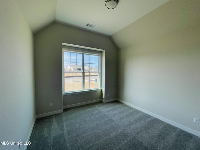 spare room featuring dark colored carpet and vaulted ceiling