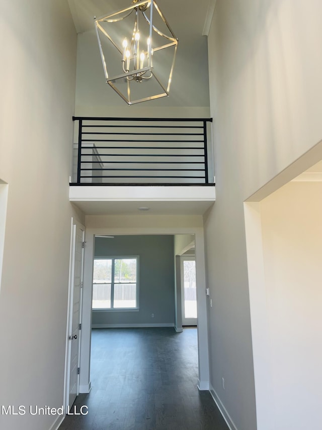 hallway with a high ceiling, dark hardwood / wood-style flooring, and an inviting chandelier