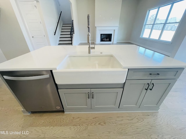 kitchen featuring a center island with sink, dishwasher, gray cabinetry, and sink