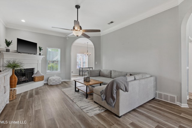 living area with visible vents, crown molding, a fireplace, arched walkways, and ceiling fan with notable chandelier