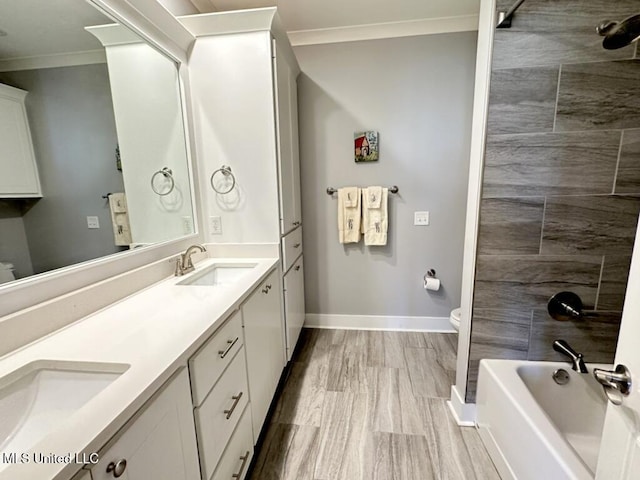 bathroom featuring baseboards, toilet, double vanity, ornamental molding, and a sink