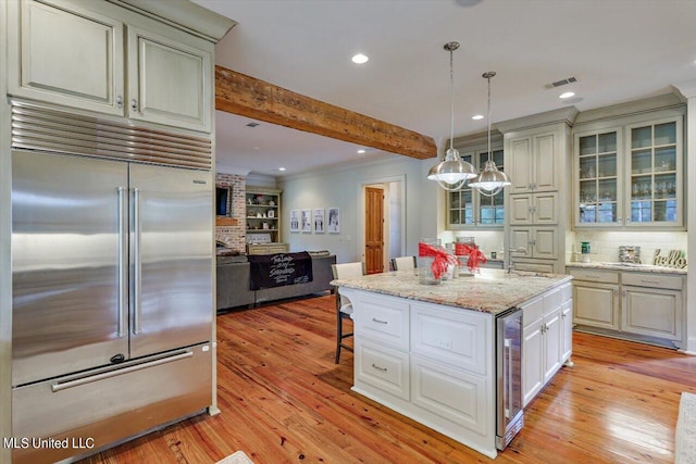 kitchen featuring light stone counters, beam ceiling, light hardwood / wood-style flooring, built in refrigerator, and hanging light fixtures