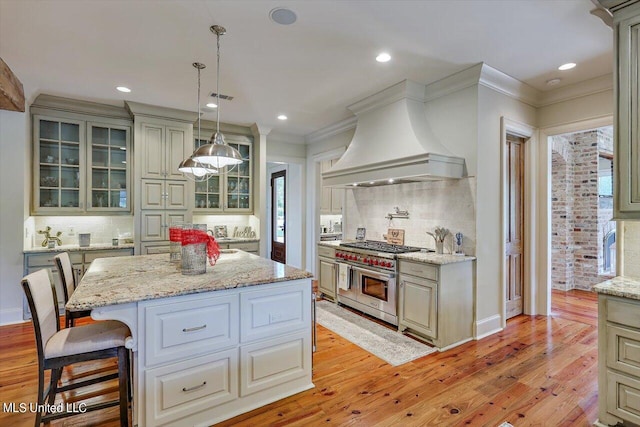 kitchen with decorative backsplash, premium range hood, double oven range, light hardwood / wood-style flooring, and a center island