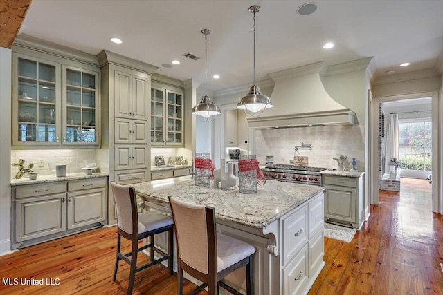 kitchen featuring decorative backsplash, custom exhaust hood, wood-type flooring, a center island, and a breakfast bar area